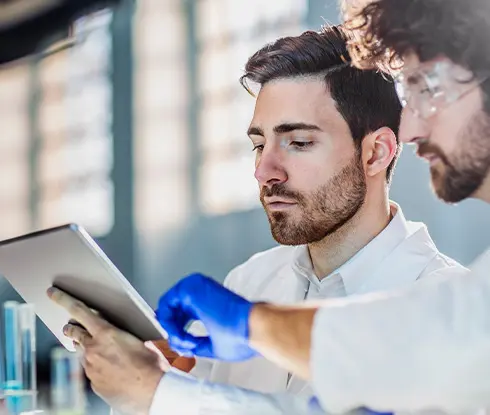 Two people wearing lab coats look over a tablet