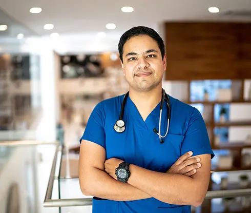 A man wearing scrubs and with a stethoscope around his neck looks at the camera for a portait. His arms are folded.