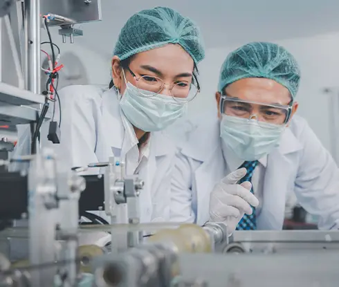 a man and a women wearing personal protective equipment looking at medical equipment.