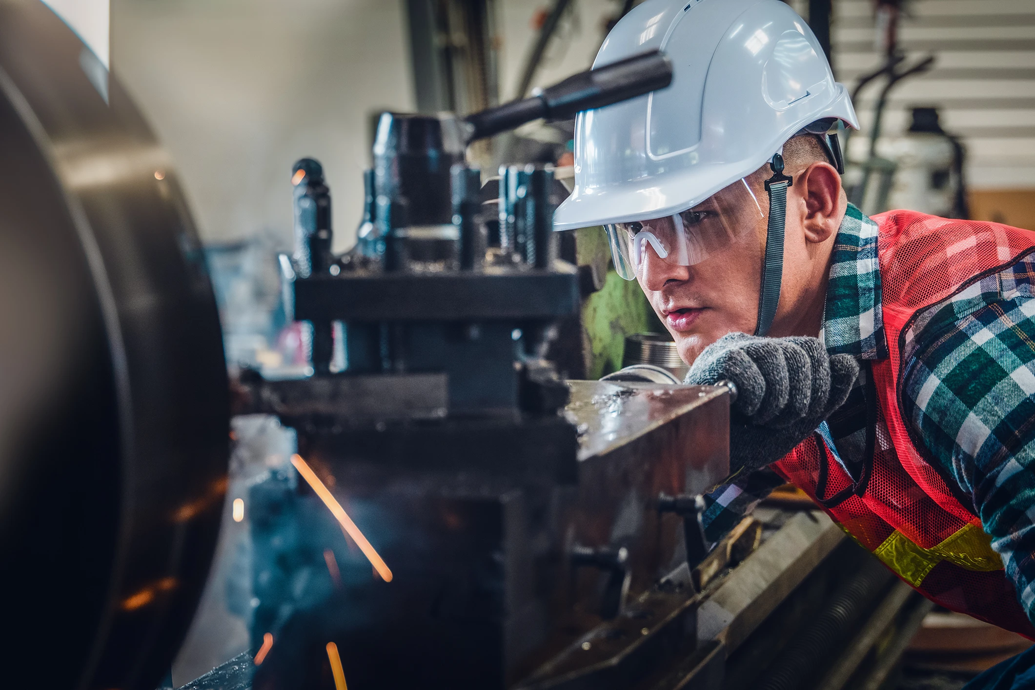 Two men wearing safety equipment look down on machining equipment