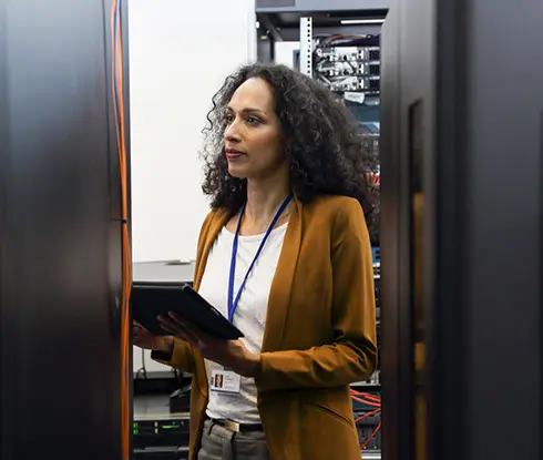 A woman wearing a cardigan and with a tablet in hand, looks at a server.